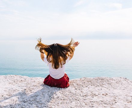 Woman sitting by the sea with her hair in the breeze